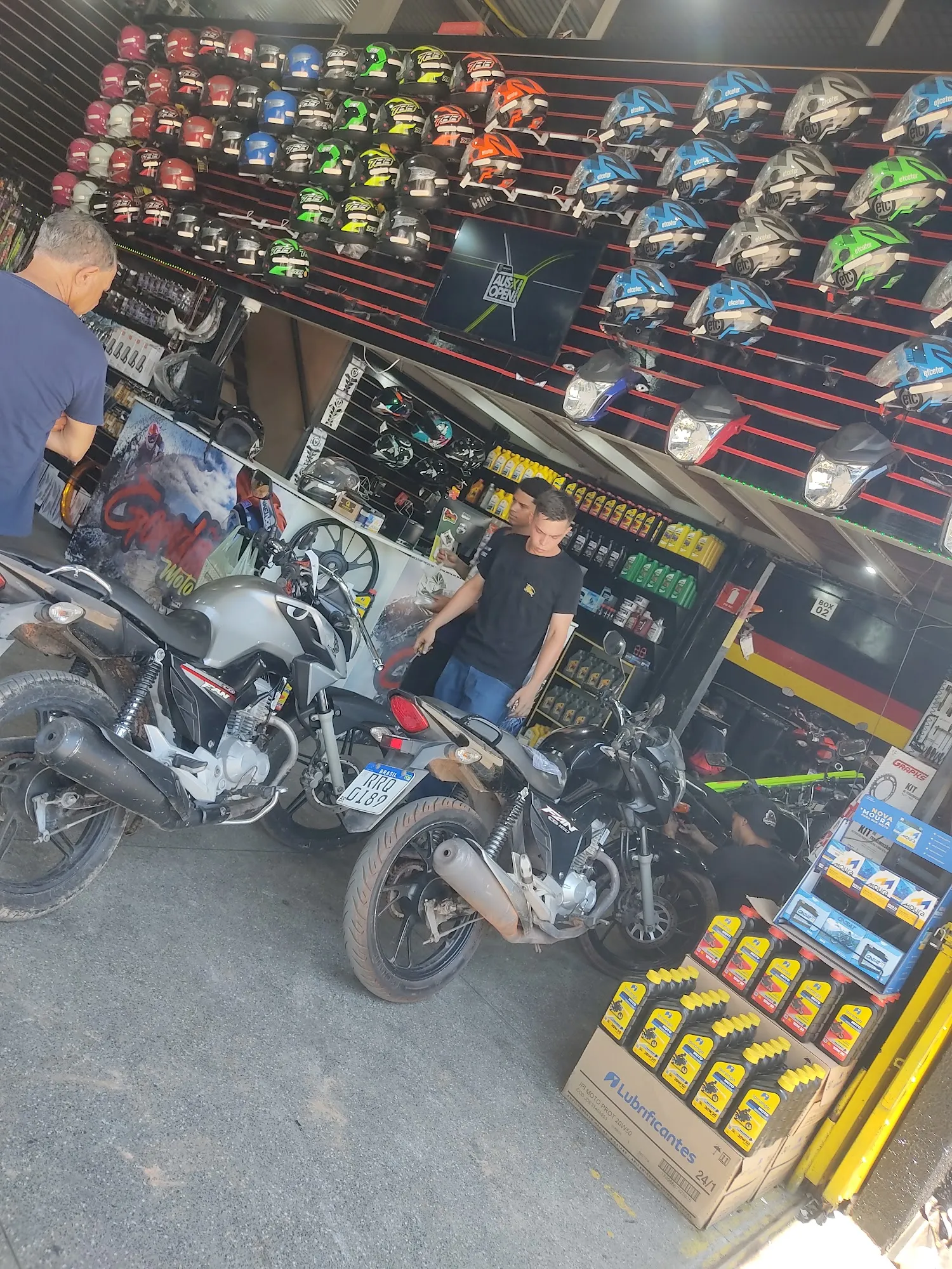 Duas motos paradas em frente ao balcão da Gordão Motos, com funcionário atendendo cliente e parede de capacetes ao fundo